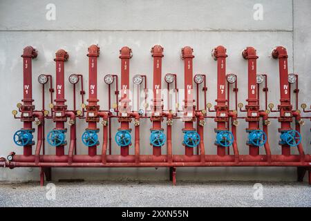 Red industrial pipes with blue valves on a concrete wall for plumbing systems. Stock Photo