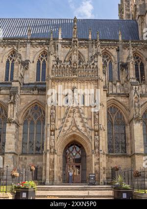 The entrance to a minster with planters in the foreground. The doorway is set in intricately carved stone with figurines on each side and above. Stock Photo