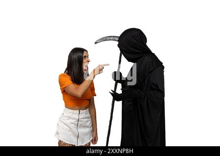 furious young woman confronts the grim reaper, dressed in a Halloween costume with a dark cloak, as he holds a scythe white background Stock Photo