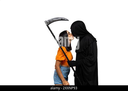 young brunette woman leans in to kiss the grim reaper, who is dressed in a Halloween costume with a dark cloak, while holding a scythe white backgroun Stock Photo