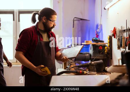 Carpenter doing last touches on piece of wood before using it for furniture assembly, sanding it with sandpaper. Woodworking expert doing woodworking process on lumber block, inspecting for damages Stock Photo