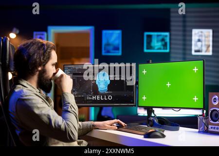 Software developer drinking coffee, watching AI on green screen PC gaining consciousness. Computer scientist consuming hot beverage, seeing artificial intelligence talking on mockup monitor Stock Photo