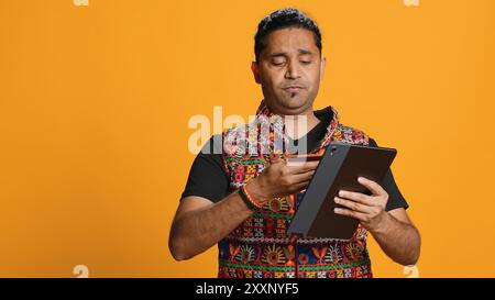 Man shakes head in disbelief after realizing lack of necessary funds while trying to shop online on tablet. Disappointed indian person gets credit card transaction rejected, studio backdrop, camera A Stock Photo