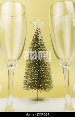 Glasses for sparkling wine, christmas tree, fake snow, gold background. Stock Photo