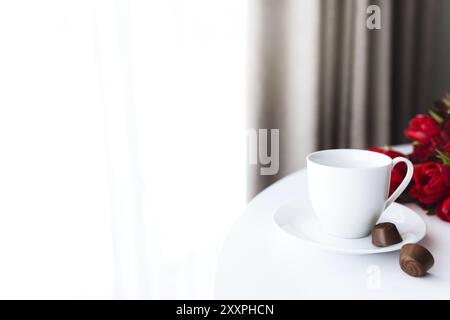 Red tulips bouquete on table, white coffee cup. Concept for greeting card for mothers day, international womans day or valentines day concept, birthda Stock Photo