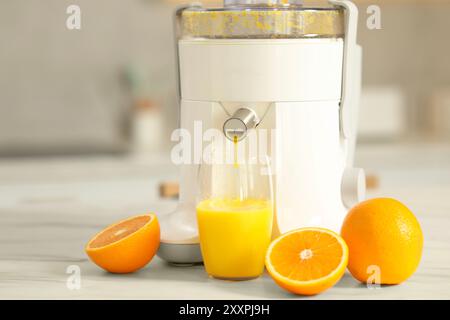 Modern juicer, oranges and glass on white marble table in kitchen Stock Photo