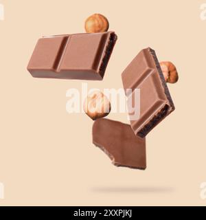 Pieces of tasty chocolate and hazelnuts falling on dark beige background Stock Photo