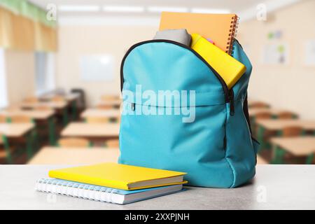 Light blue backpack with stationery on school desk in classroom Stock Photo