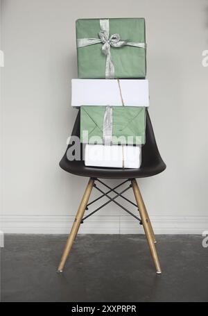 Green and white Christmas gift boxes with red ribbons on chair by the grey wall in room Stock Photo