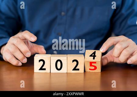 Hand flipping of 2024 to 2025 on wooden cube blocks. Starting new year 2025. Beginning and start of the new year 2024. Preparation for new year, life, Stock Photo