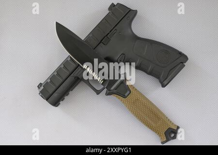 A hunting knife with a beige handle lies on a black pistol on a white surface Stock Photo