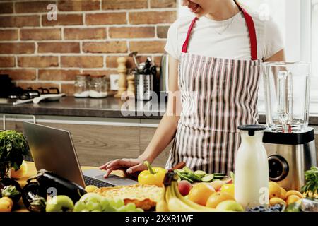 Woman using laptop at home kitchen. Girl touching touchpad with hand, searching for a recipe. Chef using pc, online food shopping on computer. Deliver Stock Photo