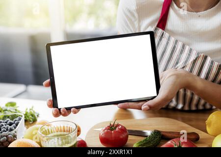 Woman hands showing digital tablet white empty blank screen mockup at kitchen. Chef using pc, present online grocery food shopping on computer. Delive Stock Photo
