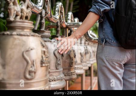 A close-up image of a female tourist in a denim jacket touching an ancient bell for luck in a Thai temple during her visit to Thailand. cultural trave Stock Photo