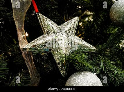 Beautiful silver-toned star Christmas ornament, angled, with mosaic style inlay and texture, amid pine needles of Christmas Tree, in close up, amid go Stock Photo