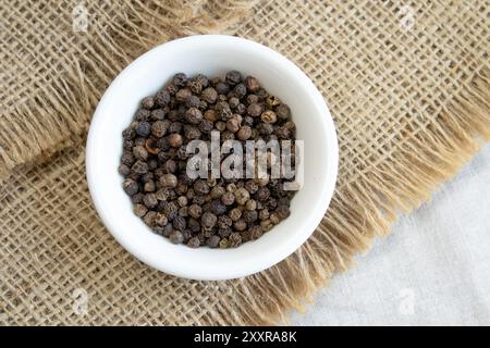 Pile of Black peppercorns Black pepper dried seeds on white plate linen background close up top view Stock Photo