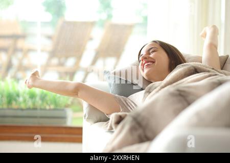 Happy woman waking up stretching arms from a nap on a sofa at home Stock Photo