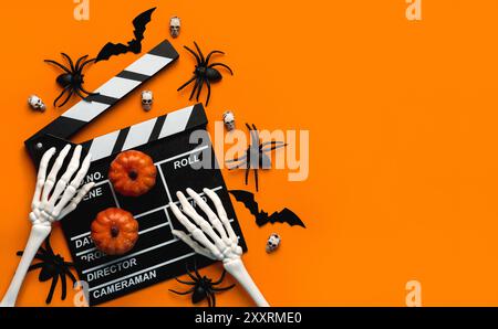 Halloween movies concept. Movie clapperboard with skeleton hands,funny halloween pumpkins and spiders with copy space for text over orange background. Stock Photo