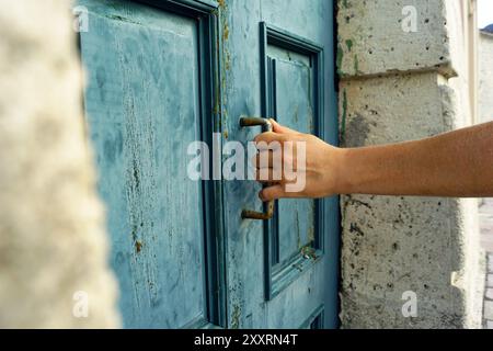 Male hand pulling the handle on a blue wooden door - close-up photo. Concept of new beginnings and discovery of the unknown. Stock Photo