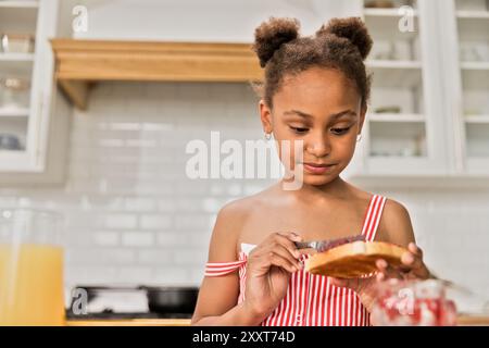 African American girl is spreading jam on bread toast in the morning Stock Photo