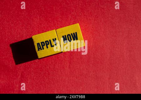 Apply now message written on yellow wooden cubes with red background. Conceptual apply now symbol. Copy space. Stock Photo