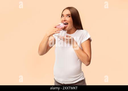 Excited Pregnant Lady Eating Donut Standing Over White Studio Background Stock Photo