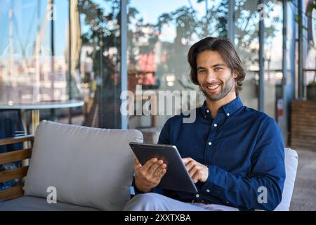 Happy young business man using tablet sitting outside office, portrait. Stock Photo