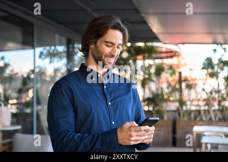 Happy young business man using mobile phone standing outdoors. Stock Photo