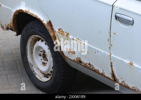 White car body with heavy rust and decay, suitable for themes of neglect, vintage cars, or wear and tear. Stock Photo