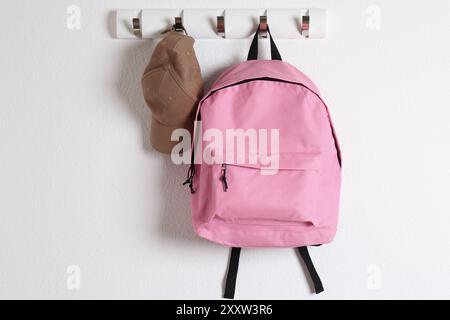 Pink backpack and cap hanging on white wall Stock Photo