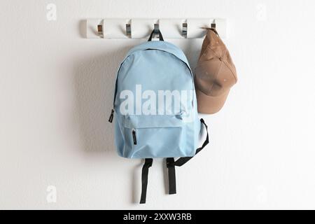 Light blue backpack and cap hanging on white wall Stock Photo