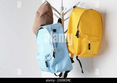 Bright backpacks and cap hanging on white wall Stock Photo