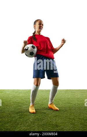 Full-length photo of young, female football athlete celebrates game-changing moment standing on stadium with ball and shouting of joy. Stock Photo