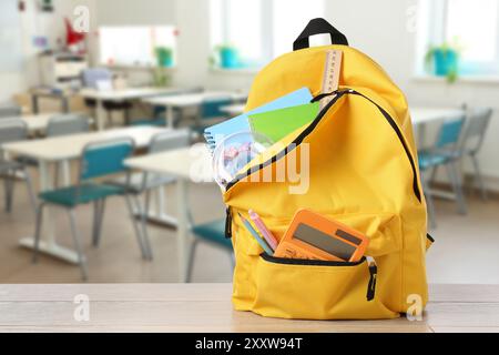 Yellow backpack with stationery on school desk in classroom. Space for text Stock Photo
