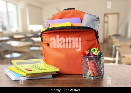 Orange backpack with stationery on school desk in classroom Stock Photo