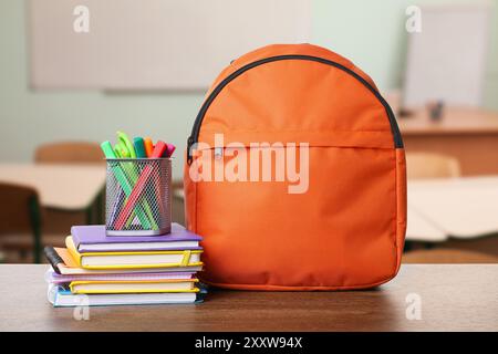 Orange backpack with stationery on school desk in classroom Stock Photo