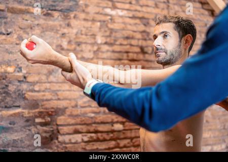 Male patient performing arm strength exercise with a small ball, guided by an osteopath. The image showcases a rehabilitation technique and assessment Stock Photo