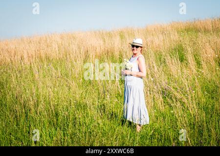 Happy mature woman with wildflowers in a tall grass field on a bright summer day. Stock Photo