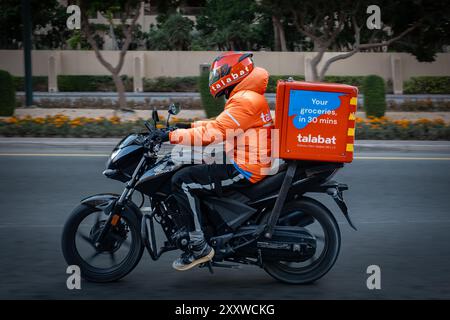 Motorcycle driver delivers food delivery. Delivery man Talabat food. Delivery rider on Dubai road making his way through busy streets. Delivery servic Stock Photo