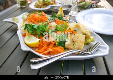White platter in fish shape with various fried fish fillets and vegetables on a large dining table with dishes and plates in an outdoor restaurant at Stock Photo