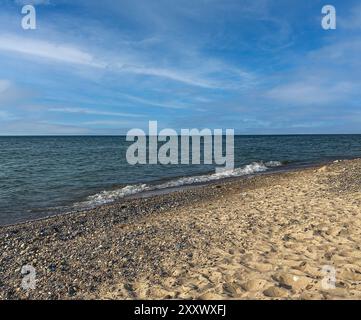 Gentle tide rolling ashore on sandy beach with wispy clouds in sky Stock Photo