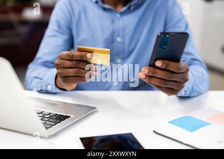Man holding credit card and smartphone for online transaction in work environment. Technology enhances convenience for digital shopping and mobile banking. Concept e-commerce and financial security. Stock Photo