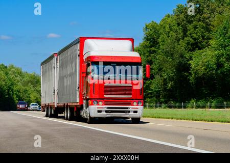 Horizontal shot of a red cab-over semi eighteen-wheeler with dual trailers.  Heat waves rising from the hot asphalt creates a blurring effect on backg Stock Photo