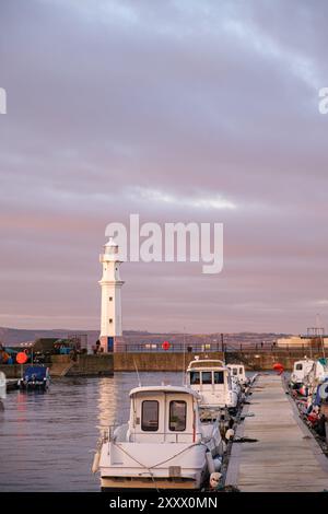 EDINBURGH - JANUARY 13, 2024: The lighthouse in Newhaven Harbour stands tall as boats rest gently by the dock, bathed in the warm hues. Stock Photo