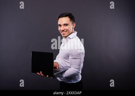 Image of young cheerful businessman holding and using laptop isolated over dark background Stock Photo