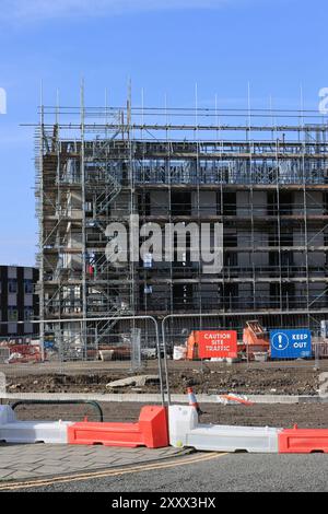 Construction site with red and white barriers and steel security fencing in foreground and scaffolding covered building development in background uk Stock Photo