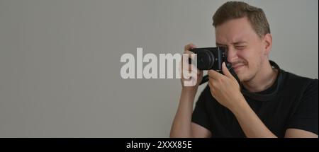 Young man with a photocamera. The photographer uses a camera to take a photo looking through lens. Professional photographing concept. Design banner b Stock Photo