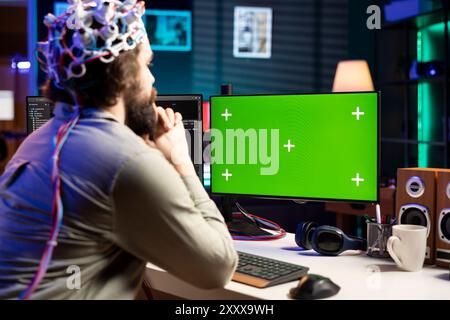 Neuroscientist using EEG headset to upload his mind into green screen computer, attaining immortality. Software developer using mockup PC, experimenting with transferring consciousness into cyberspace Stock Photo