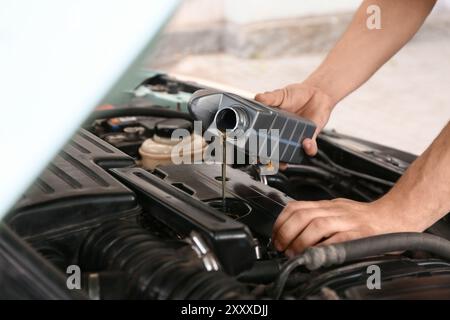 Male mechanic pouring car oil into engine outdoors, closeup Stock Photo