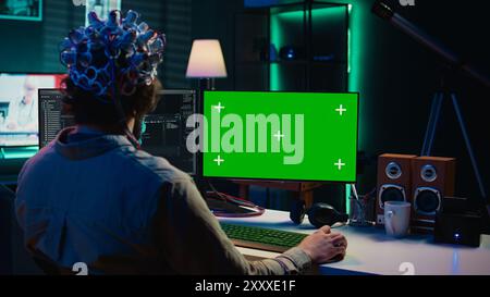 IT admin coding and using EEG headset to upload brain into mockup computer, gaining immortality. Neuroscientist engineering transhumanism experiment on isolated screen PC, camera B Stock Photo